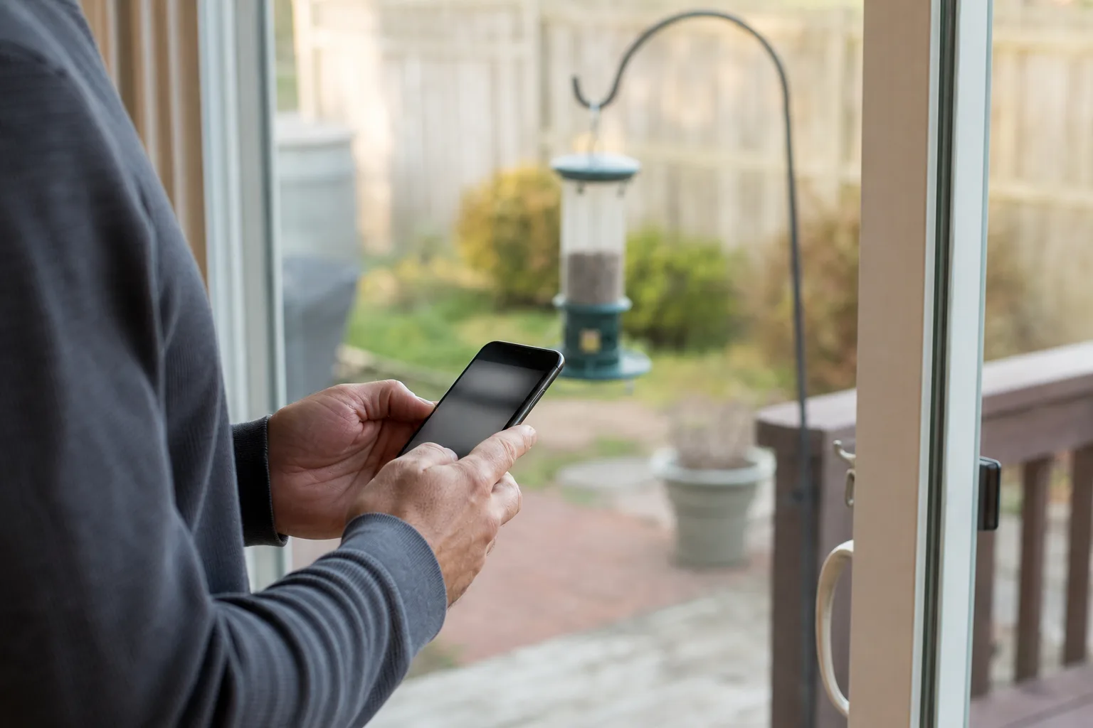 A person checking a phone near a patio door before installing a feeder